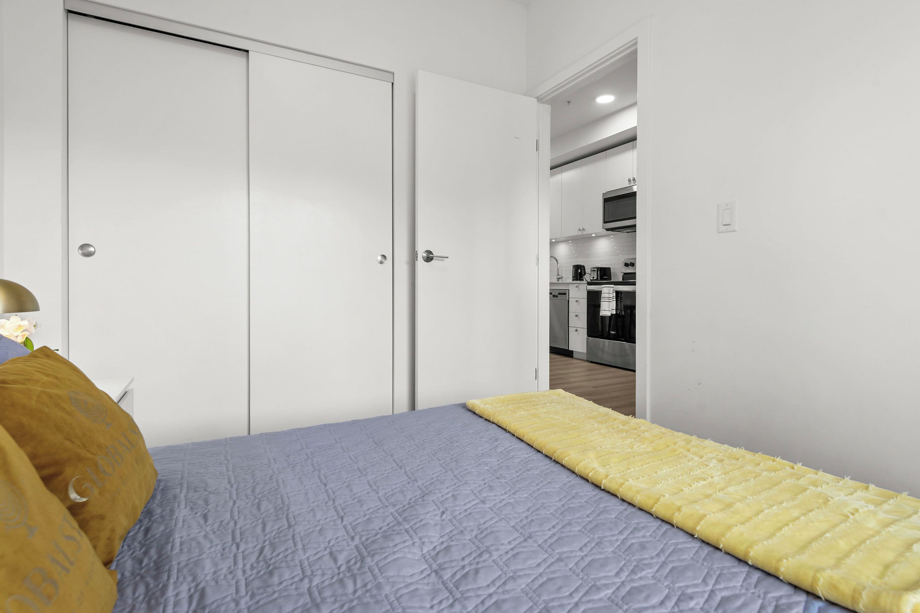 Quarto com cama, colcha amarela e mesa de cabeceira com abajur.