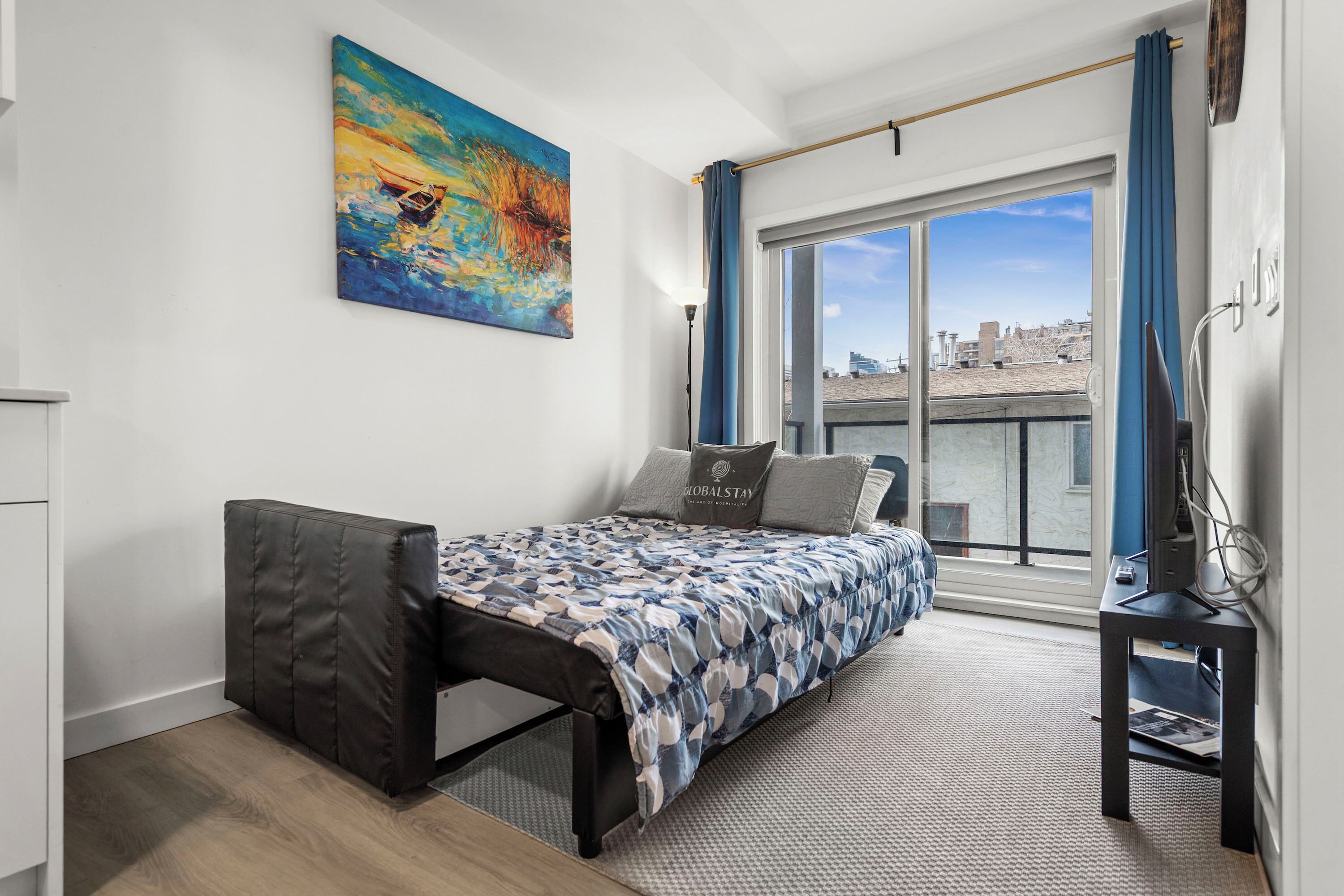 A modern bedroom with a bed, a desk, and a large window with a view of the city.