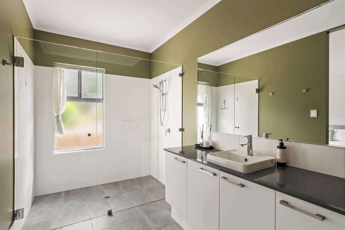 A modern bathroom with a large mirror, two sinks, and a shower.