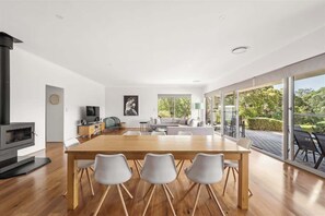 Un salon moderne avec une table à manger en bois, des chaises blanches, une cheminée, un canapé et une grande porte vitrée donnant sur un jardin.