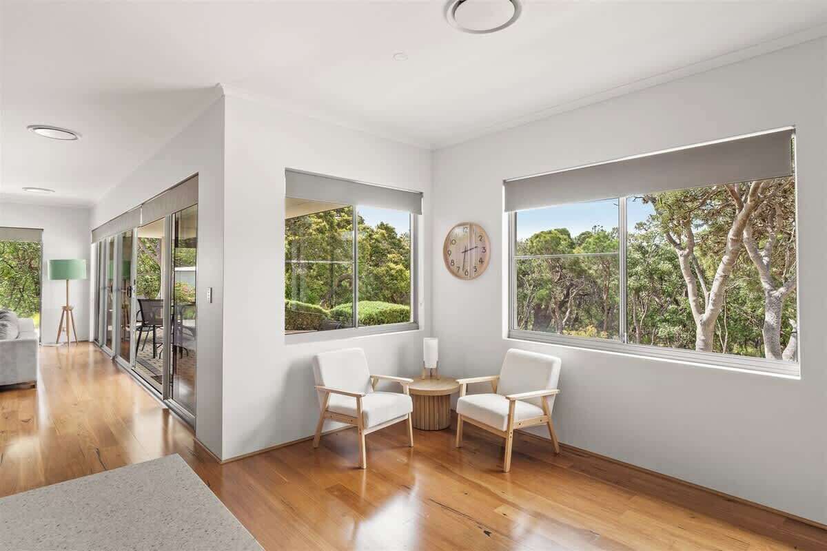 A spacious room with large windows, a round table, two chairs, and a clock on the wall.