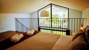 Een slaapkamer met een groot bed, uitzicht op groen en een balkon met een hekwerk.