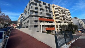 Un edificio residencial de varios pisos con balcones, una entrada porticada y un pavimento rojo.