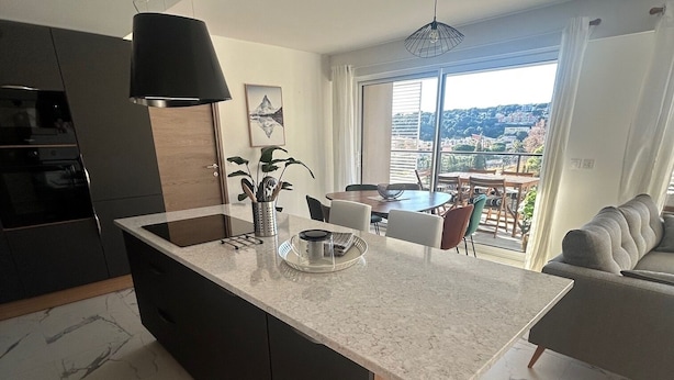 Una cocina moderna con una isla grande, armarios oscuros y vistas a un balcón.