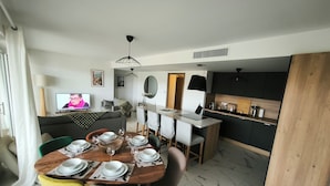 Una sala de estar moderna con comedor, cocina y un televisor mostrando a una persona.