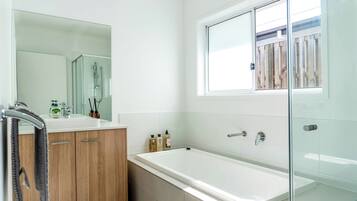 A modern bathroom with a glass shower enclosure, a large mirror, and a window with a view of a wooden fence.