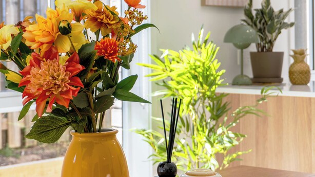 Une table ornée d’un vase jaune rempli de fleurs, d’un petit récipient en verre contenant une bougie et d’un ananas décoratif.