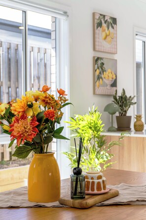 Une table ornée d’un vase jaune rempli de fleurs, d’un petit récipient en verre contenant une bougie et d’un ananas décoratif.