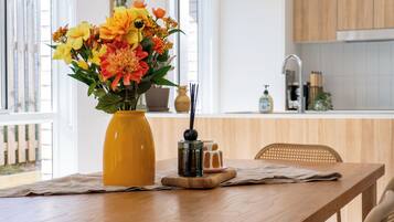 A wooden table with a yellow vase of flowers, a small black container, and a glass of water.