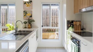 Une cuisine moderne dotée d’un évier en acier inoxydable, d’un four encastré et d’une fenêtre donnant sur une terrasse en bois.
