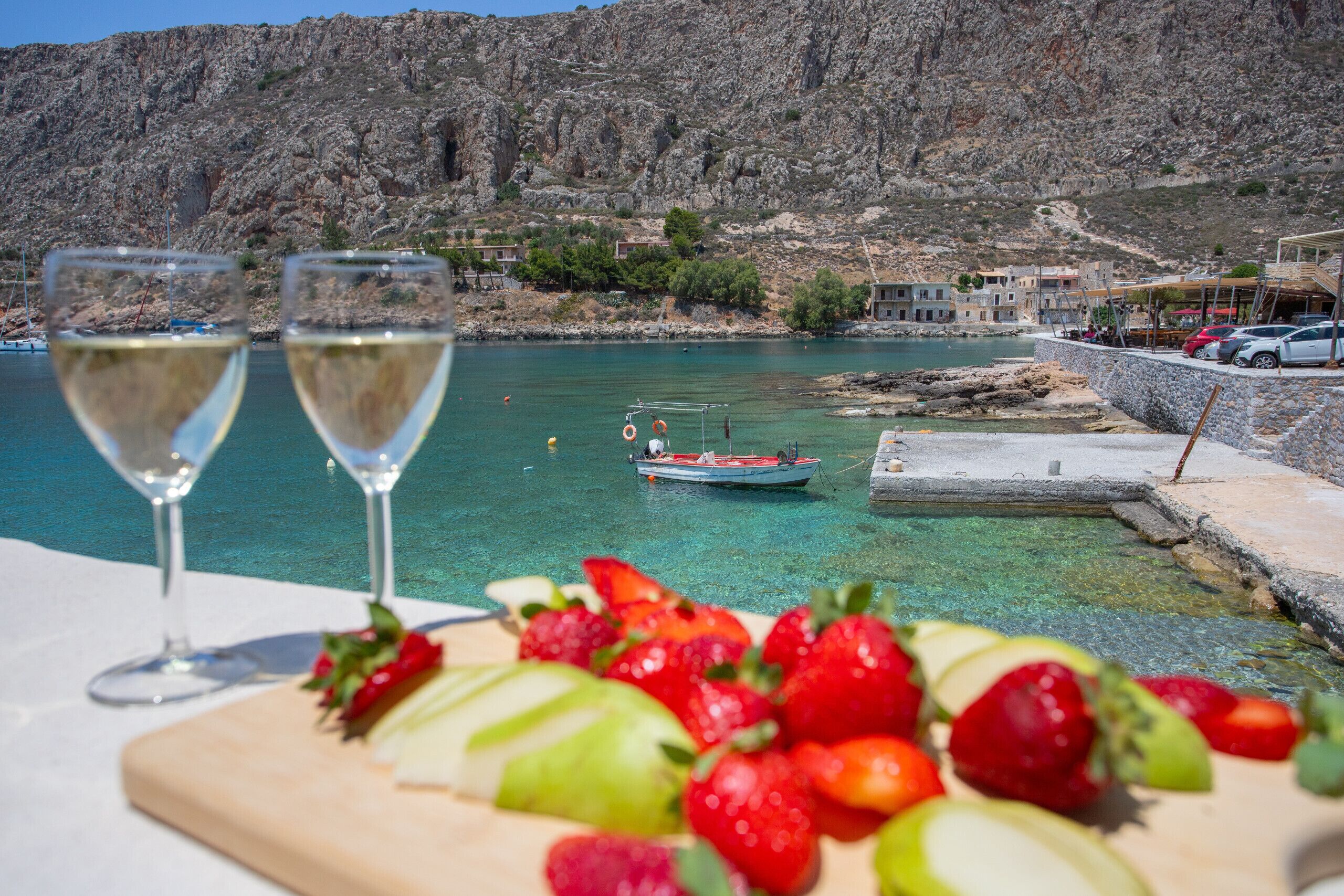 A table with two glasses of white wine and a platter of sliced fruits.