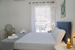 A neatly made bed with white linens, a bedside table with a lamp, and a view of the outdoors through a large window. - Gerolimin Captain Antonis (East Mani)