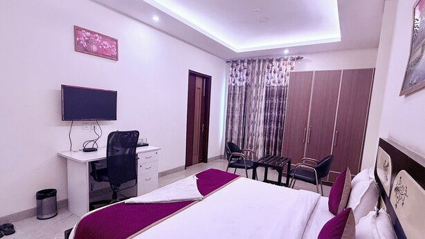 A hotel room with a bed, desk, chair, TV, wardrobe, and curtains. - STAR INN (Gurugram)