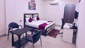 A bedroom with a bed, desk, chairs, a ceiling fan, an air conditioner, and a painting on the wall. - STAR INN (Gurugram)