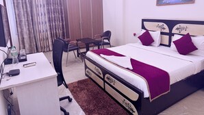 A bedroom with a bed, desk, chairs, and a painting on the wall. - STAR INN (Gurugram)