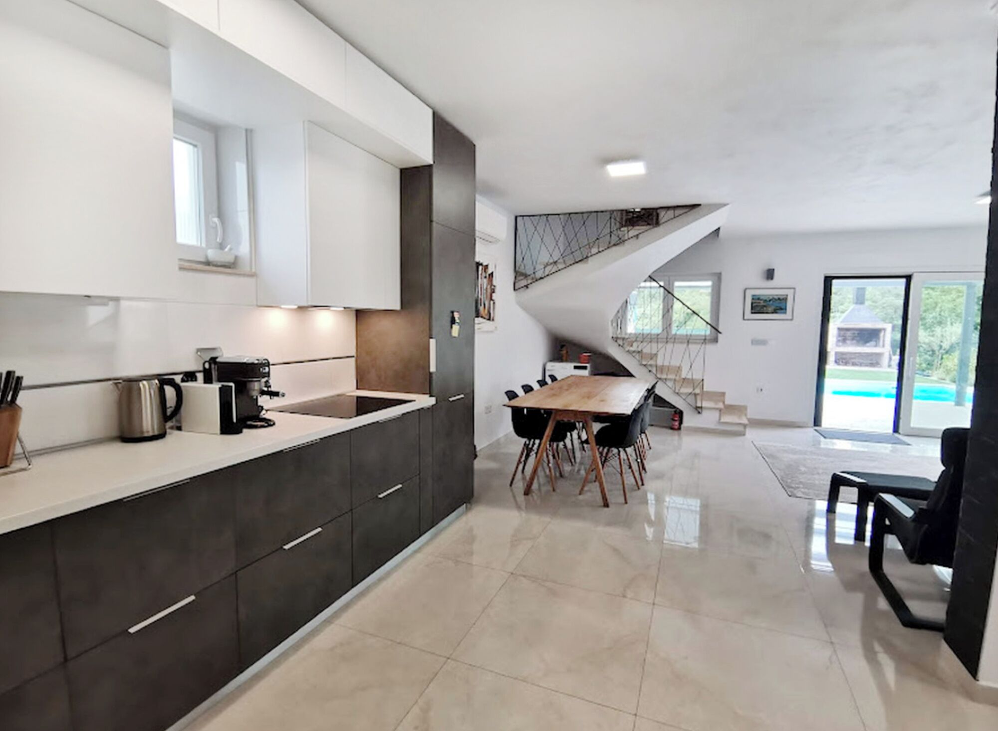 A modern kitchen with dark cabinetry, a white countertop, and a dining area with a wooden table and chairs.