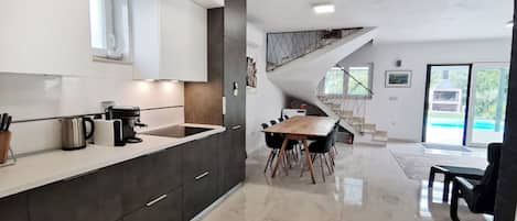 A modern kitchen with dark cabinetry, a white countertop, and a dining area with a wooden table and chairs.