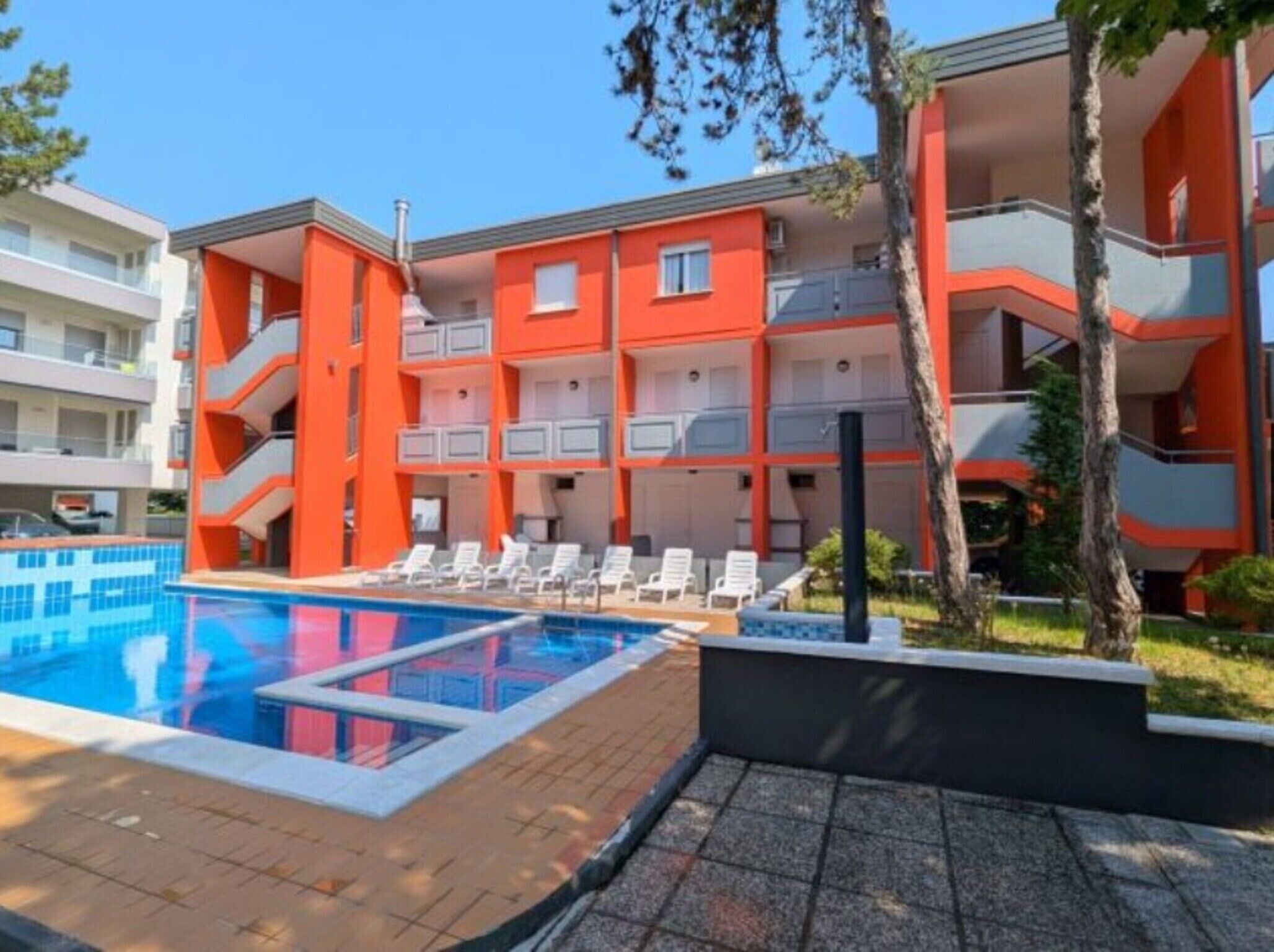A multi-story hotel with orange and white exterior walls, a swimming pool, and sun loungers.