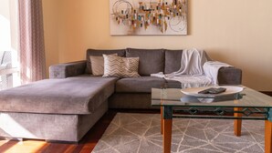 Een moderne woonkamer met een hoekbank, een glazen salontafel en een vloerkleed met een geometrisch patroon.