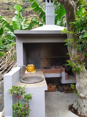Un petit espace cuisine extérieur comprenant un évier, un pot jaune et un four en briques.