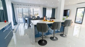 Uma área de refeições moderna com piso de mármore, uma mesa branca e banquetas de bar cinzas.