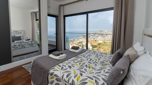 Quarto moderno com uma cama grande, vista da cidade e porta deslizante para uma varanda.