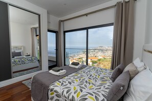 A modern bedroom with a large bed, a view of the city, and a sliding door leading to a balcony. - Vila Valeria seen over the Port of Funchal (Funchal)