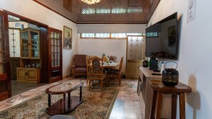Un salón tradicional con suelo de madera, un sofá, una mesa de comedor con sillas, un armario y un televisor.