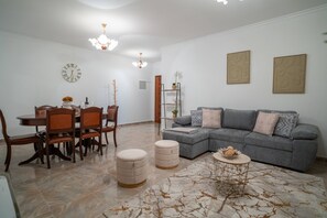 Ein modernes Wohnzimmer mit Essbereich, ausgestattet mit einem grauen Sofa, einem Holzesstisch und zwei Hocker.