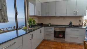 A kitchen with white cabinets, a black countertop, and a view of the sea through a large window.