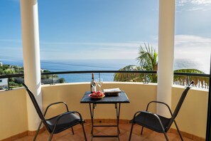 Ein Balkon mit zwei Stühlen, einem Tisch, einem Buch, einem Weinglas und einer Schale Obst.