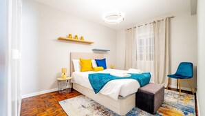 Een moderne slaapkamer met een bed, nachtkastjes, een stoel en een raam met gordijnen.