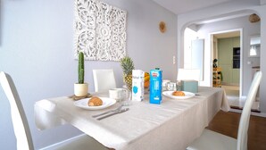 Een eethoek met een tafel gedekt voor twee personen, met een cactuss, ananas, vruchtensap en een bord met gebak.