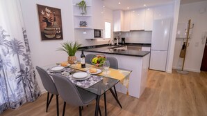 Una cuina moderna amb armaris blancs, una illa central i una zona de menjador amb taula i cadires de vidre.