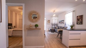 Un saló modern amb un sofà, una taula de centre i objectes decoratius. Es veu una zona de cuina amb un taulell i armaris.