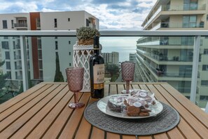 En balkon med et træbord, en vinflaske, to glas og en tallerken med kage og småkager.