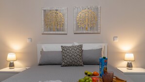 Een netjes opgemaakt bed met een schaal fruit en sap, twee wandlampen en twee kunstwerken in lijsten aan de muur.