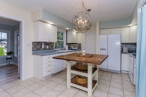 Cocina con armarios blancos, una isla de madera y una lámpara colgante.