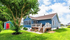 A blue house with a front porch, a small garden, and a shed in the background. - Located in Keenwick Sound with Backyard Oasis: fire pit, bar, & TV; Community Pool & Boat/Kayak launch (Selbyville)