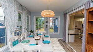 A dining area with a white table set for four, a hanging rattan light fixture, and a view through the window to the outside. - Located in Keenwick Sound with Backyard Oasis: fire pit, bar, & TV; Community Pool & Boat/Kayak launch (Selbyville)