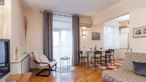 A modern living room with a sofa, a dining table with chairs, a small round table with a candle, and a TV. - Spacious apartments near Pobedy Square (Minsk)