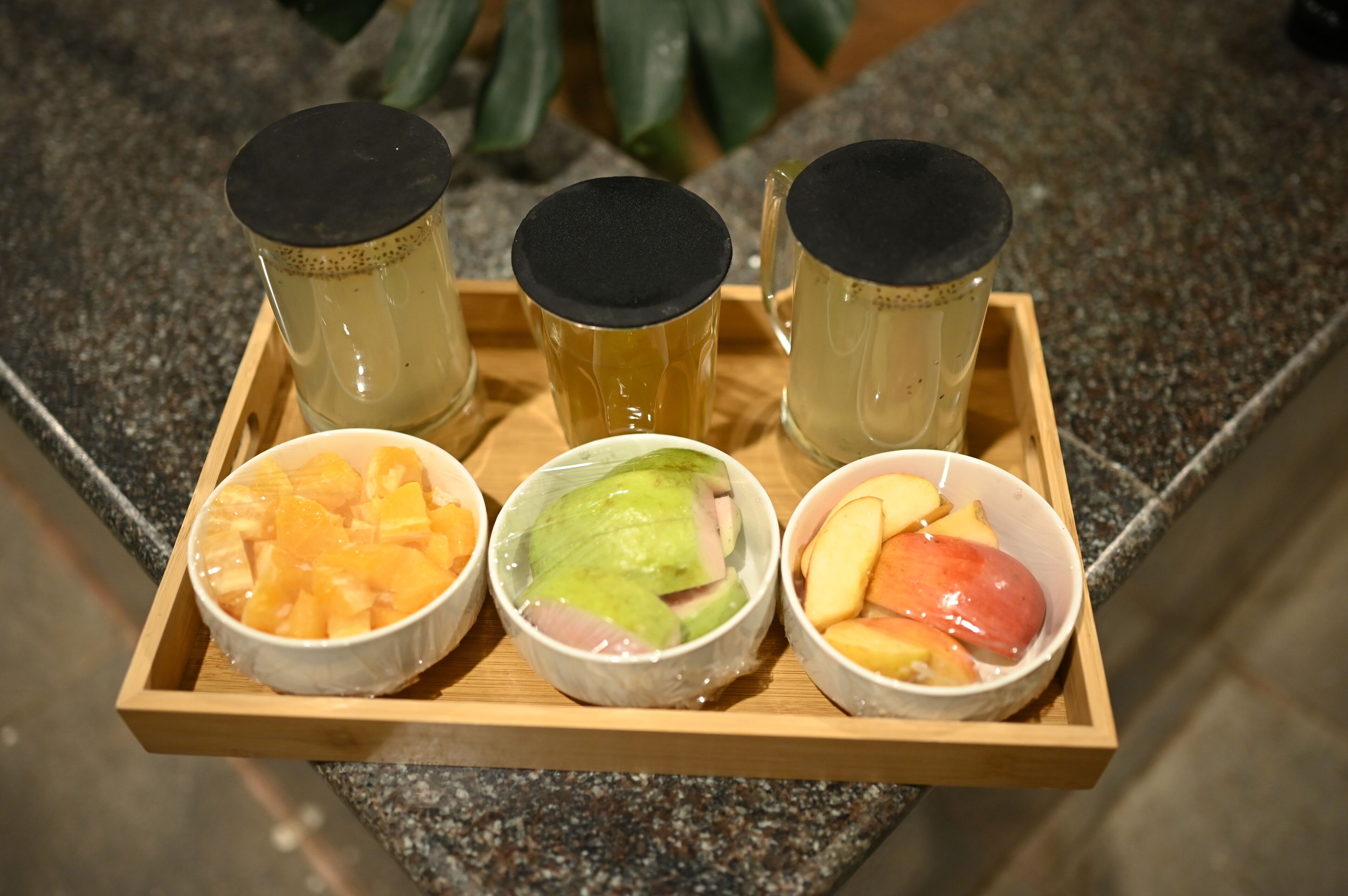 Una bandeja con tres tazas de té y tres tazones de fruta.