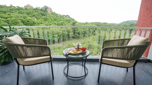 Un balcon avec deux fauteuils en osier, une petite table sur laquelle se trouvent une théière, des verres et un plateau de thé, donnant sur un paysage verdoyant et luxuriant.