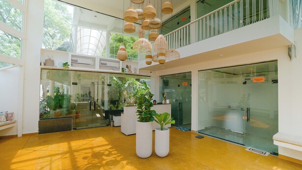 Un hall d’entrée spacieux, doté d’un haut plafond, de grandes fenêtres et d’un design moderne. On y trouve des plantes en pot et des luminaires suspendus.