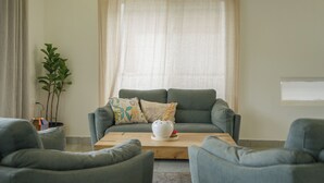 Un salon avec un canapé gris, deux fauteuils assortis, une table basse en bois et une plante en pot.
