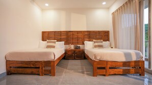 Une chambre d’hôtel avec deux lits en bois, une table de chevet avec un téléphone et une petite table, ainsi qu’une grande fenêtre avec des rideaux.