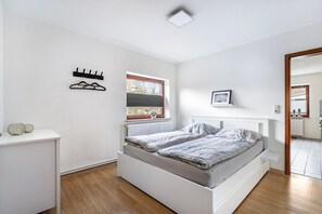 Une chambre à coucher comprenant un lit, une fenêtre, un radiateur, une étagère avec des objets décoratifs et un porte-manteau.