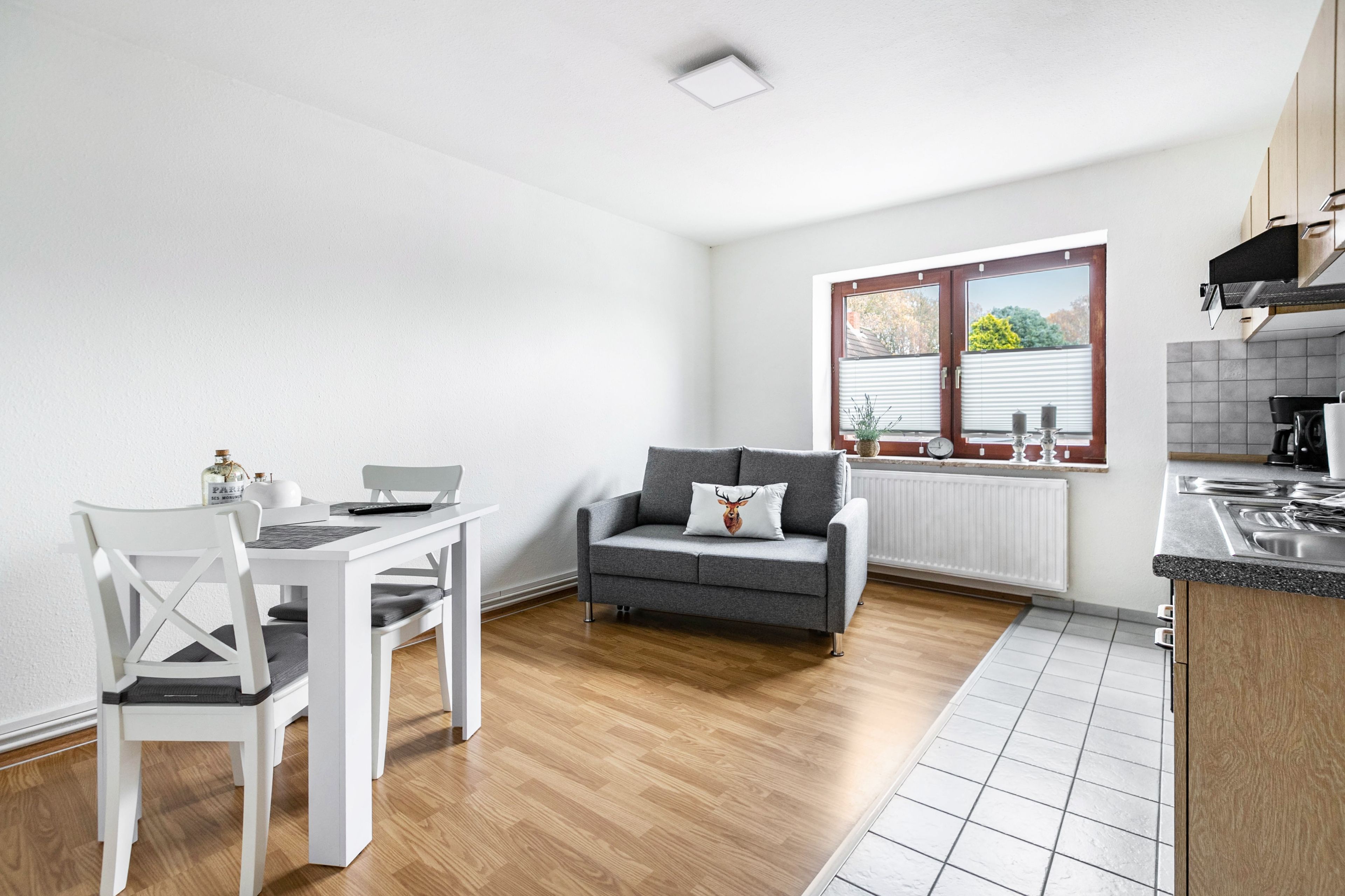 A modern kitchen with a dining area, a grey sofa, and a window with blinds.