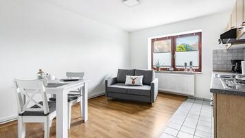 A modern kitchen with a dining area, a grey sofa, and a window with blinds.