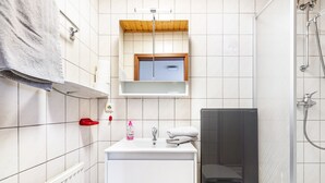 Ein Badezimmer mit einem weißen Waschbecken, einem Spiegel darüber, einem Handtuchhalter und einer Duschkabine.